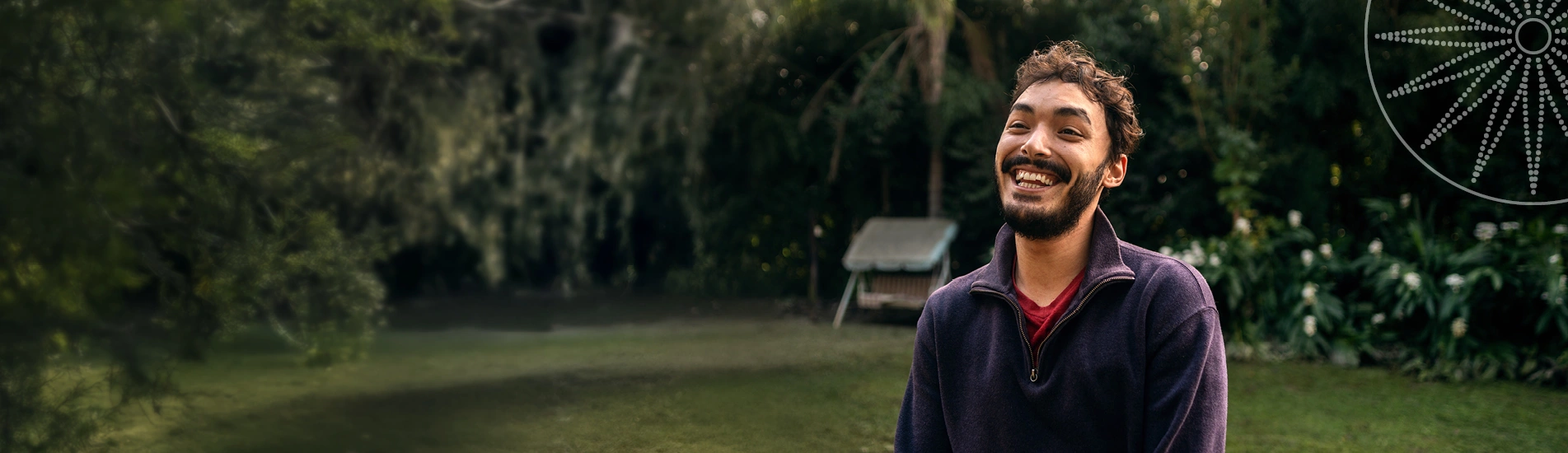 A young man with short hair and a beard wearing a purple sweater smiling big